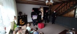 Czworo policjantów z prezentami, w czapkach Świętego Mikołaja, stoją naprzeciwko podopiecznych z placówki opiekuńczej.
