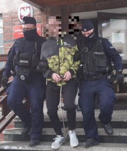 Na zdjęciu dwóch policjantów wyprowadzają z budynku policji zatrzymanego skutego w kajdankach.