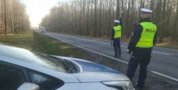 Na zdjęciu droga i dwóch policjantów stojących obok radiowozu i zatrzymujących nadjeżdżający pojazd.