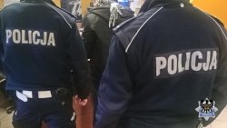 Na zdjęciu policjanci pilnują zatrzymanego mężczyzny.