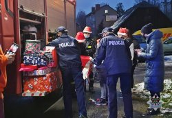 Na zdjęciu policjantka, policjant i strażak przekazują wręczają prezenty dzieciom.