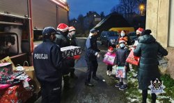 Na zdjęciu policjantka, policjant i strażak przekazują wręczają prezenty dzieciom - kolejne zdjęcie.