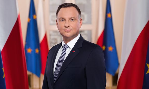 Na zdjęciu znajduje się Prezydent Rzeczypospolitej Polskiej na tle flag Polski i Unii Europejskiej