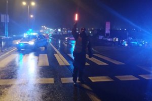 Zdjęcia robione nocą, na których widać policjant ruchu drogowego kierującego ruchem na drodze. W tle radiowozy policyjne.