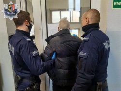 Na zdjęciu dwóch umundurowanych policjantów prowadzi zatrzymanego mężczyznę (zdjęcie z tyłu).