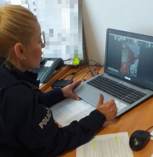 Na zdjęciu policjantka siedzi przed komputerem i rozmawia online z innymi osobami których twarze wyświetlają się w okienkach na ekranie.