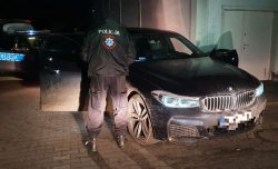 Na zdjęciu policjant stoi obok odzyskanego z kradzieży BMW. W tle widać radiowóz.