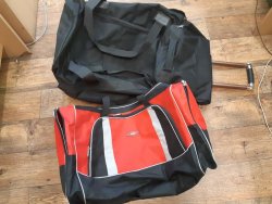 Na zdjęciu widać dwie torby podróżne, jedna jest koloru czarnego a druga czarno-czerwono-biała