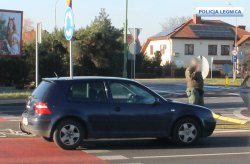 granatowy samochód osobowy vw golf stojący na ulicy w środku miasta, a przed nim stoi mężczyzna