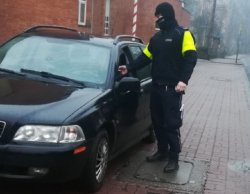 policjant kontroluje  trzeźwość zatrzymanego kierowcy auta osobowego przy pomocy alkomatu