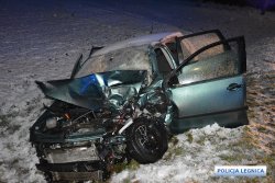 Na zdjęciu samochód osobowy stoi z otwartymi drzwiami od strony kierującego w polu na śniegu i jest uszkodzony po wypadku drogowym; zniszczona karoseria i wszystkie elementy pojazdu znajdujące się pod pokrywą silnika.