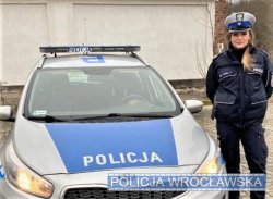 Na zdjęciu policjantka, która wykonywała pilotaż stojąca przy oznakowanym radiowozie.