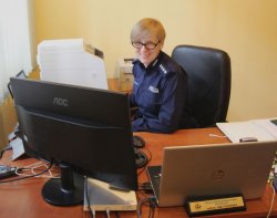 Na zdjęciu nadkomisarz Ewa Tuszyńska siedząca przy biurku, przed komputerem. Pani Ewa uśmiechnięta patrzy w obiektyw.