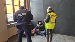 Policjant wraz z pracowniczką MOPS-u rozmawiają z dwoma osobami bezdomnymi na terenie dworca.