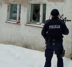 Na zdjęciu policjant sprawdza opuszczony dom z wybitymi szybami, miejsca, gdzie mogą przebywać osoby potrzebujące pomocy.