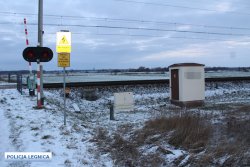 Na zdjęciu zaśnieżony przejazd kolejowy wraz z sygnalizatorem i urządzeniem transformatorowym umieszczonym przy torach.