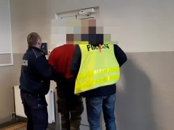 Na zdjęciu widać dwóch policjantów doprowadzających do pomieszczenia osobę ( mężczyznę) podejrzanego o dokonanie kradzieży z włamaniem do garażu.