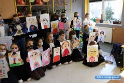 Na zdjęciu stojące w klasie dzieci, które w rękach trzymają namalowane własnoręcznie plakaty przedstawiające ich babcie lub dziadków.