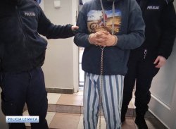 zatrzymany mężczyzna stojący w spodniach z kajdankami na rękach z dwoma policjantami