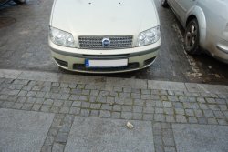 Na zdjęciu widać przód samochodu osobowego przy krawężniku. Na chodniku znajduje się kamień.
