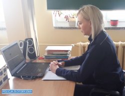 Na zdjęciu widać umundurowaną policjantkę, która siedzi przy biurku, przed nią stoi komputer, prowadzi zajęcia z młodzieżą online.