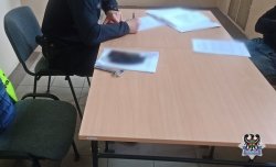 zatrzymany mężczyzna podpisuje dokumenty przy stoliku