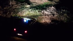 Radiowóz policyjny oświetla światłami drogowymi miejsce znalezienia niewybuchu (pora wieczorowo-nocna).
