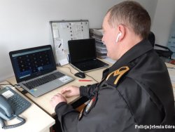 na zdjęciu widać strażnika miejskiego siedzącego przy biurku przy komputerze i prowadzącego zajęcia
