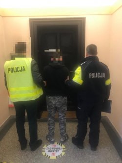 Dwóch policjantów prowadzi zatrzymanego nieletniego, kierują się do drzwi