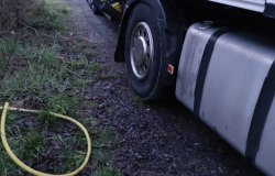 na zdjęciu widać fragment pojazdu ciężarowego i jego bak paliwa oraz leżący na trawie wąż