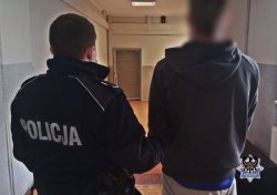 na zdjęciu widać policjanta umundurowanego, który prowadzi zatrzymanego mężczyznę