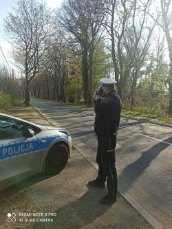 policjant stoi koło drogi i mierzy prędkość przy pomocy radaru
