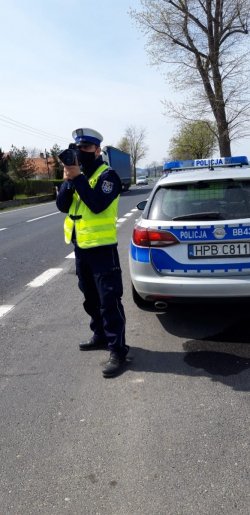 policjant stoi koło drogi i mierzy prędkość przy pomocy radaru