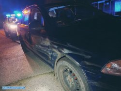 zatrzymany porysowany samochód osobowy a zanim radiowóz na sygnałach świetlnych