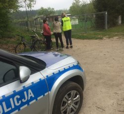 3 osoby w tym niemundurowana policjanta stoją przed bramą działkową