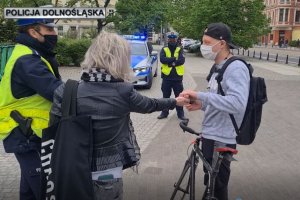 Policjant rozmawia z rowerzystą dając mu rowerowe gadżety