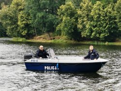 Umundurowani funkcjonariusze płyną łodzią służbową po rzece.