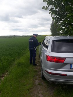 Nieoznakowany radiowóz na boku drogi podczas kontroli z policjantem sprawdzajacym dokumenty