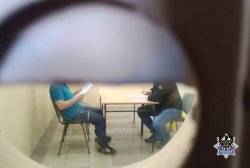na zdjęciu widać przez wizjer w drzwiach siedzącego na przesłuchaniu policjanta i zatrzymanego mężczyznę