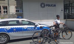 na zdjęciu widać policjanta na rowerze oraz radiowóz i budynek komendy