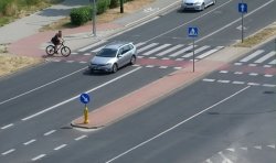 zdjęcie zrobione z góry, widać samochód mijający przejazd dla rowerów i wjeżdżającego rowerzystę oraz inny samochód