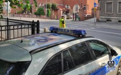 na zdjęciu widać radiowóz i policjanta stojącego przy drodze, widać budynki i drogę
