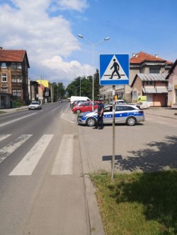 na zdjęciu widać fragment drogi, obok stoi radiowóz i policjant, widać znaki drogowe i przejście dla pieszych