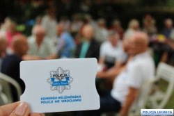 Karta z napisem Komenda Wojewódzka Policji we Wrocławiu, a w tle siedzącę starsze osoby.
