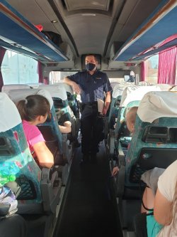 na zdjęciu widać wnętrze autokaru a w nim siedzące dzieci i przemawiającego policjanta