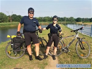 na zdjęciu policjanci stoją przy rowerach, w kaskach na głowach, w tle widać zieleń