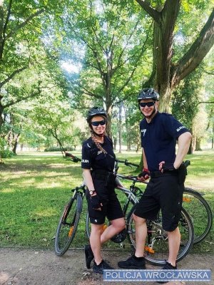 na zdjęciu policjanci stoją przy rowerach, w kaskach na głowach, w tle widać zieleń