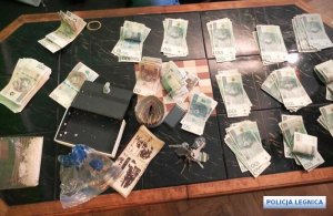 Na stole znajdują się narkotyki i pieniądze w postaci papierowych banknotów oraz waga elektroniczna.