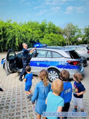 policjantka prezentuje radiowóz, dzieci wpatrzone stoją na dworze