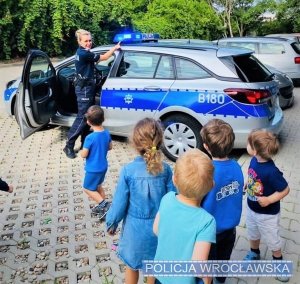 policjantka prezentuje radiowóz na dworze, dzieci patrzą